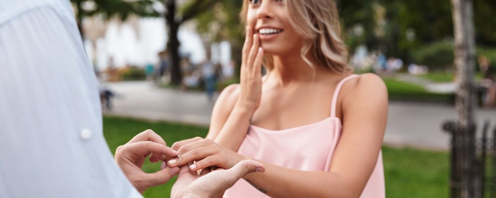 Hombre proponiendo matrimonio a una mujer sorprendida en un parque al atardecer.