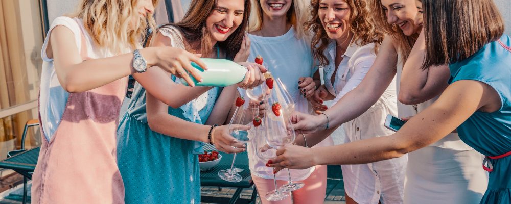 Grupo de amigas celebrando una despedida de soltera, riendo y sirviendo champán al aire libre.