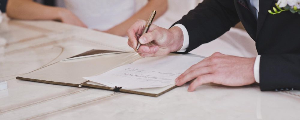 Testigo firmando el acta matrimonial en una boda con una pluma, simbolizando su rol esencial en la ceremonia nupcial.