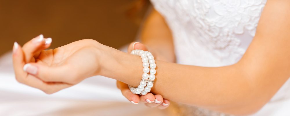 Novia ajustando su brazalete de perlas, un accesorio elegante que complementa su vestido de boda y realza su estilo.