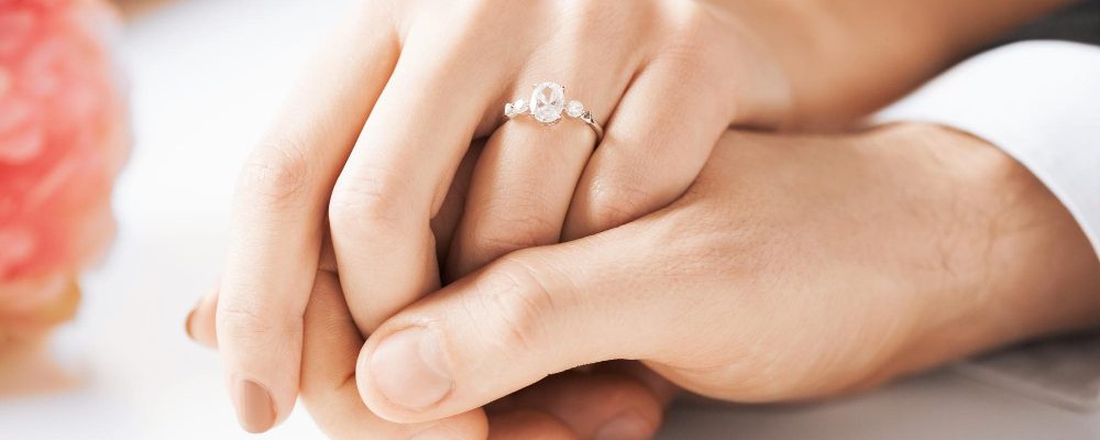 Manos entrelazadas mostrando un anillo de compromiso, simbolizando la variedad de estilos para encontrar la joya perfecta.
