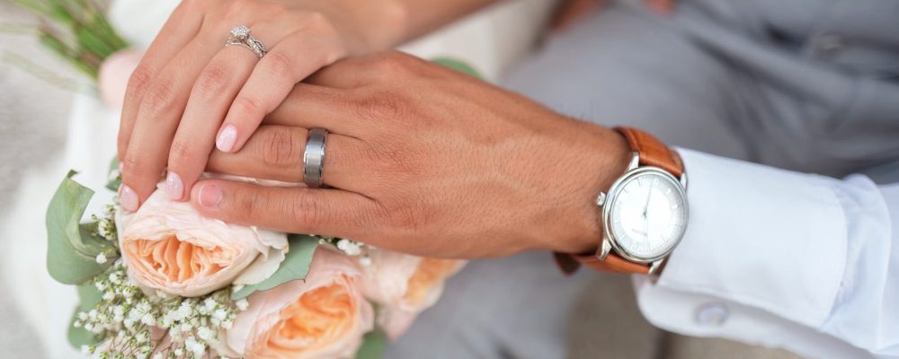 Pareja intercambiando anillos durante la ceremonia con un oficial de bodas leyendo en el fondo, simbolizando el compromiso matrimonial.