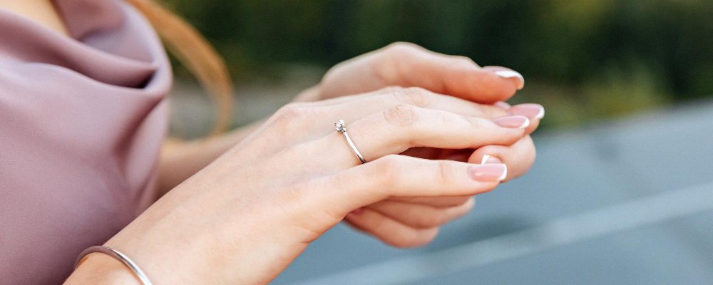 Manos delicadas de una mujer con un elegante anillo de promesa, simbolizando compromiso y amor, en un fondo borroso.