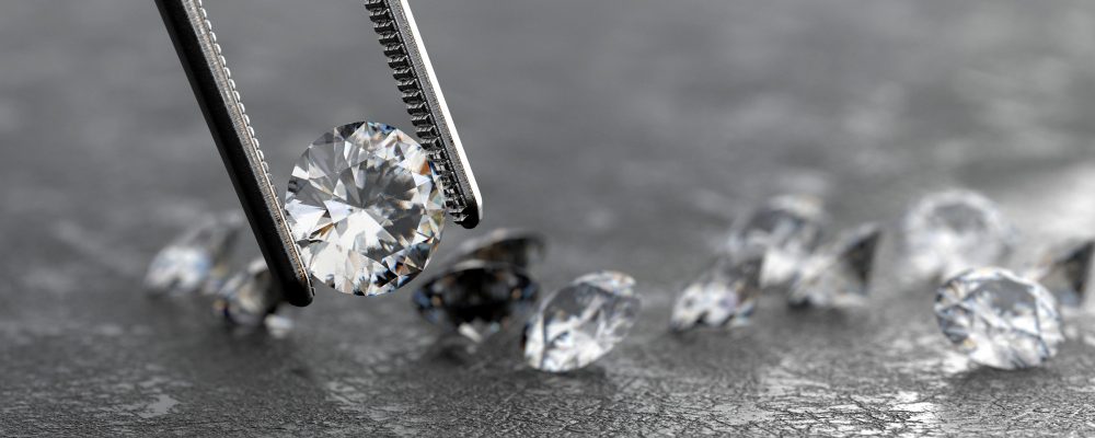 Pinzas de gemólogo sosteniendo un diamante brillante y reluciente con otros diamantes dispersos sobre una superficie oscura, representando la precisión en la medición de quilates en la joyería.