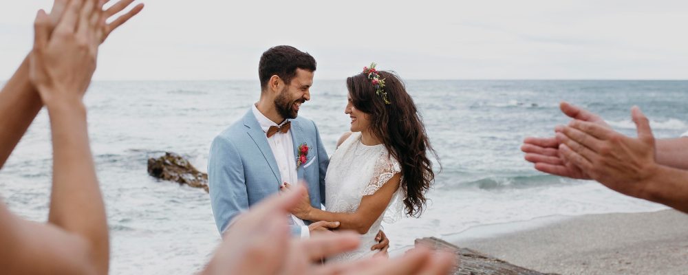 Novios recién casados recibiendo un aplauso de los invitados en su boda en la playa, con el océano como telón de fondo.
