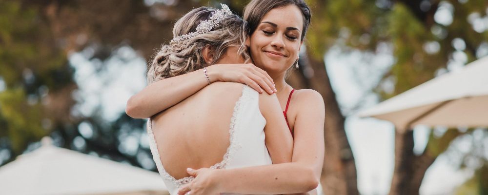 La novia abrazando a su hermana, ambas vestidas elegantemente para la boda, con árboles de fondo.