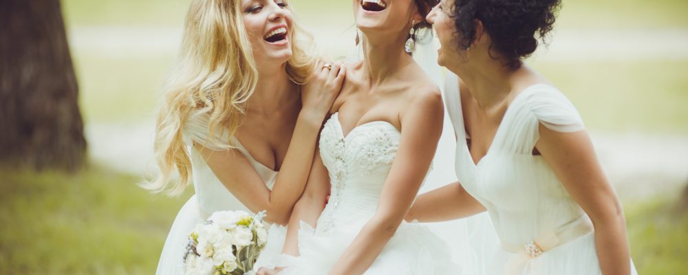 Novia riendo con sus dos damas de honor al aire libre en una boda.