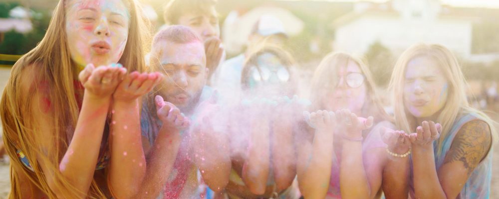 Grupo de amigos soplando polvos de colores en una celebración al aire libre.